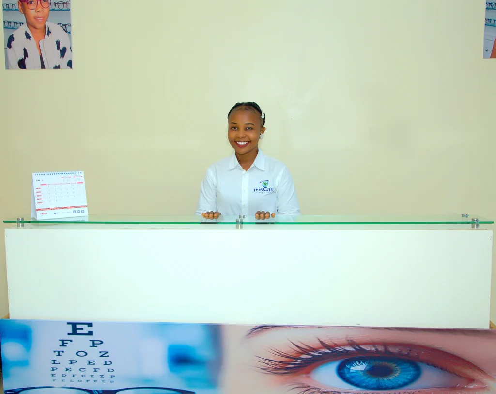 Friendly customer service representative smiling behind the reception counter at IrisCare Eye Clinic, welcoming corporate clients for professional workplace eye screening and vision care services.